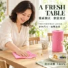 Pink Household Cleaning Cloth for Wiping Dining Tables A woman wipes breakfast crumbs from a wooden dining table with a pink patterned cleaning cloth, beside a pink cloth roll, cup and plate.