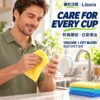 Yellow Kitchen Cleaning Cloth for Wiping Drinking Glasses A man in a green shirt wipes a clear drinking glass with a yellow patterned cleaning cloth, with folded colored cloths beside the kitchen sink.